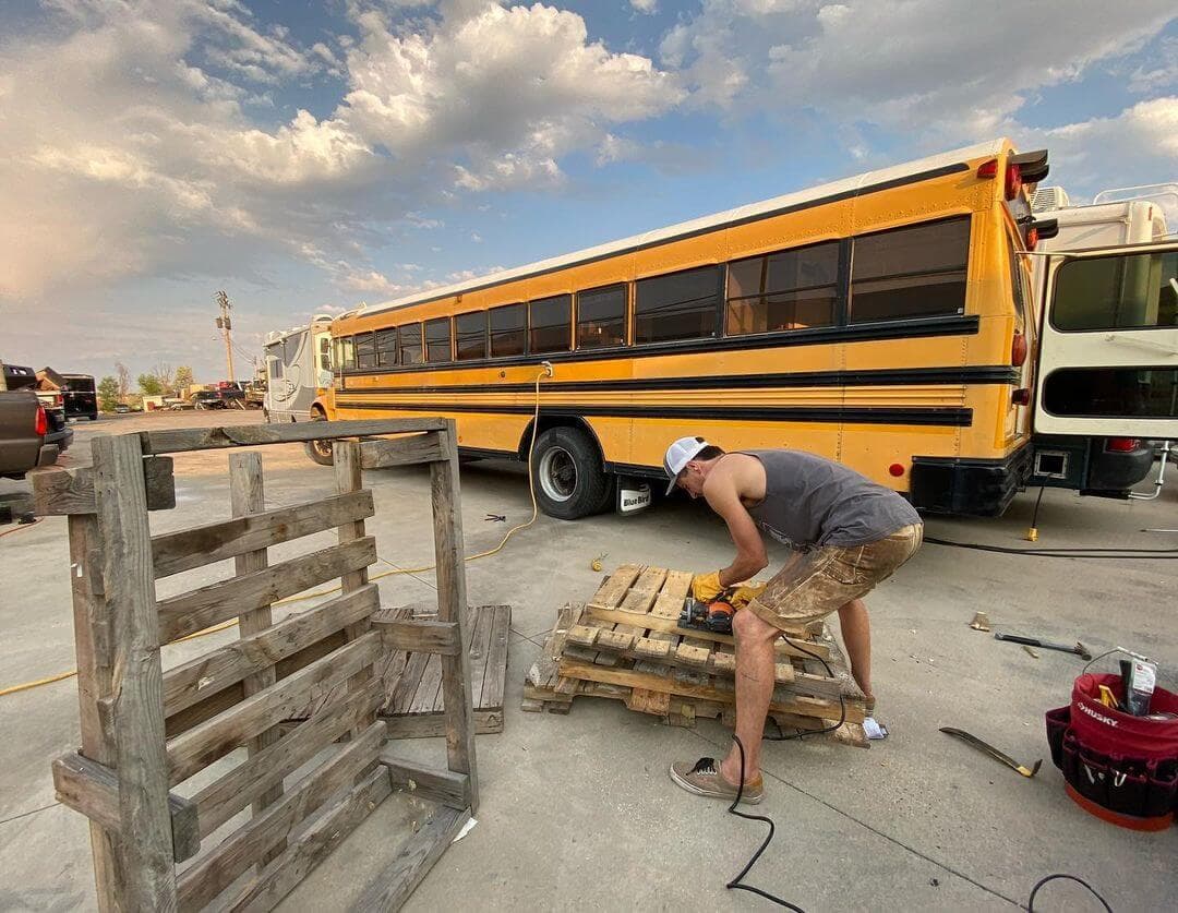 An RV Service Club tech building out a school-bus (skoolie) RV conversion at sunset